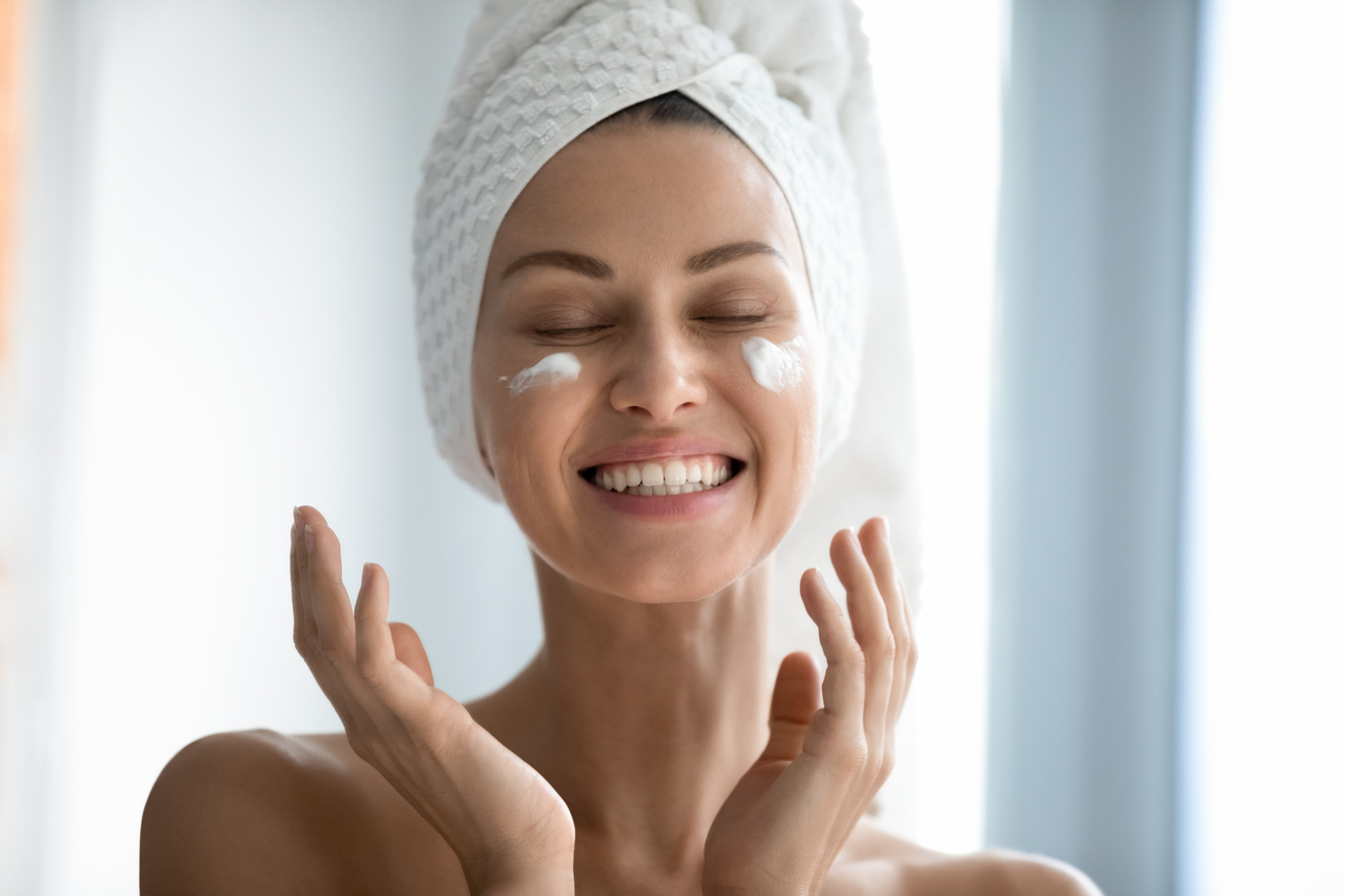 Beautiful lady laughing while applying skincare creme.